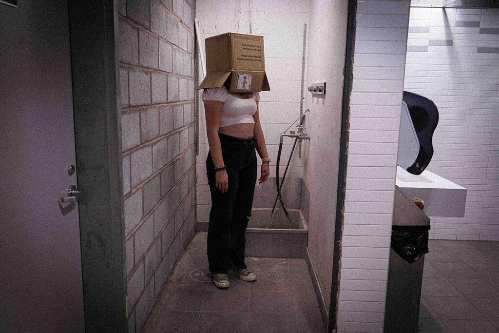 Person wearing a box on their head standing ominously in a public restroom