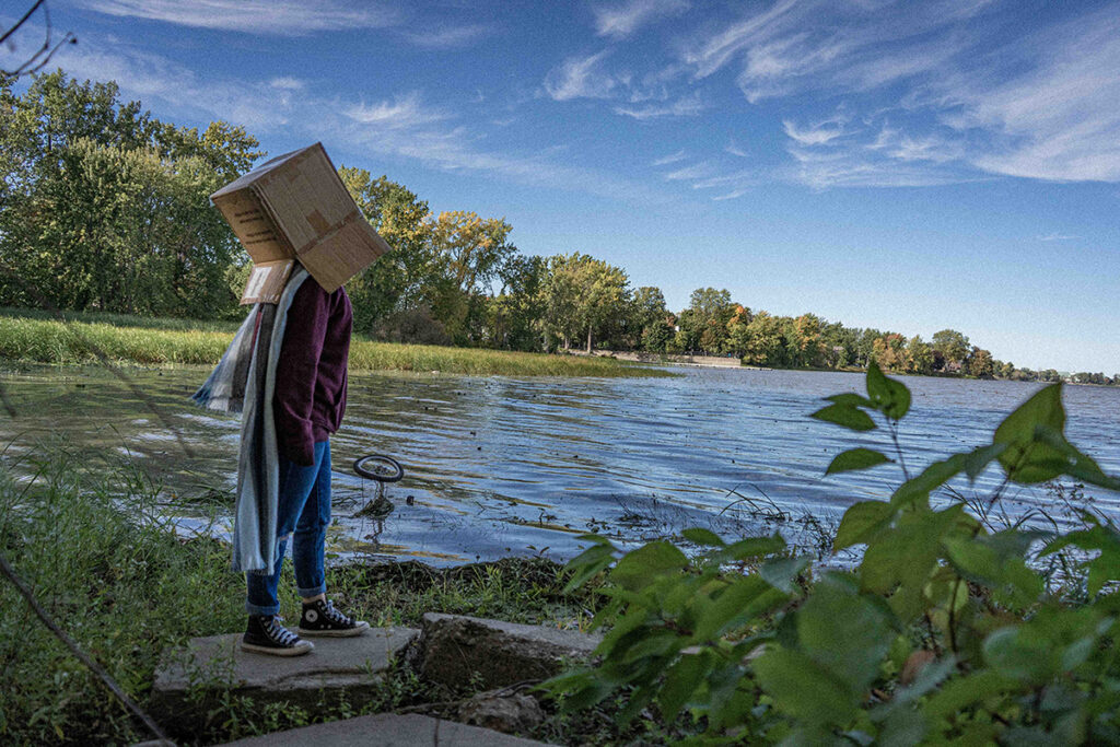 person with a box on their head looking over a dirty lake