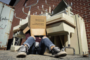 person with box on their head sitting in front of a pile of old desks